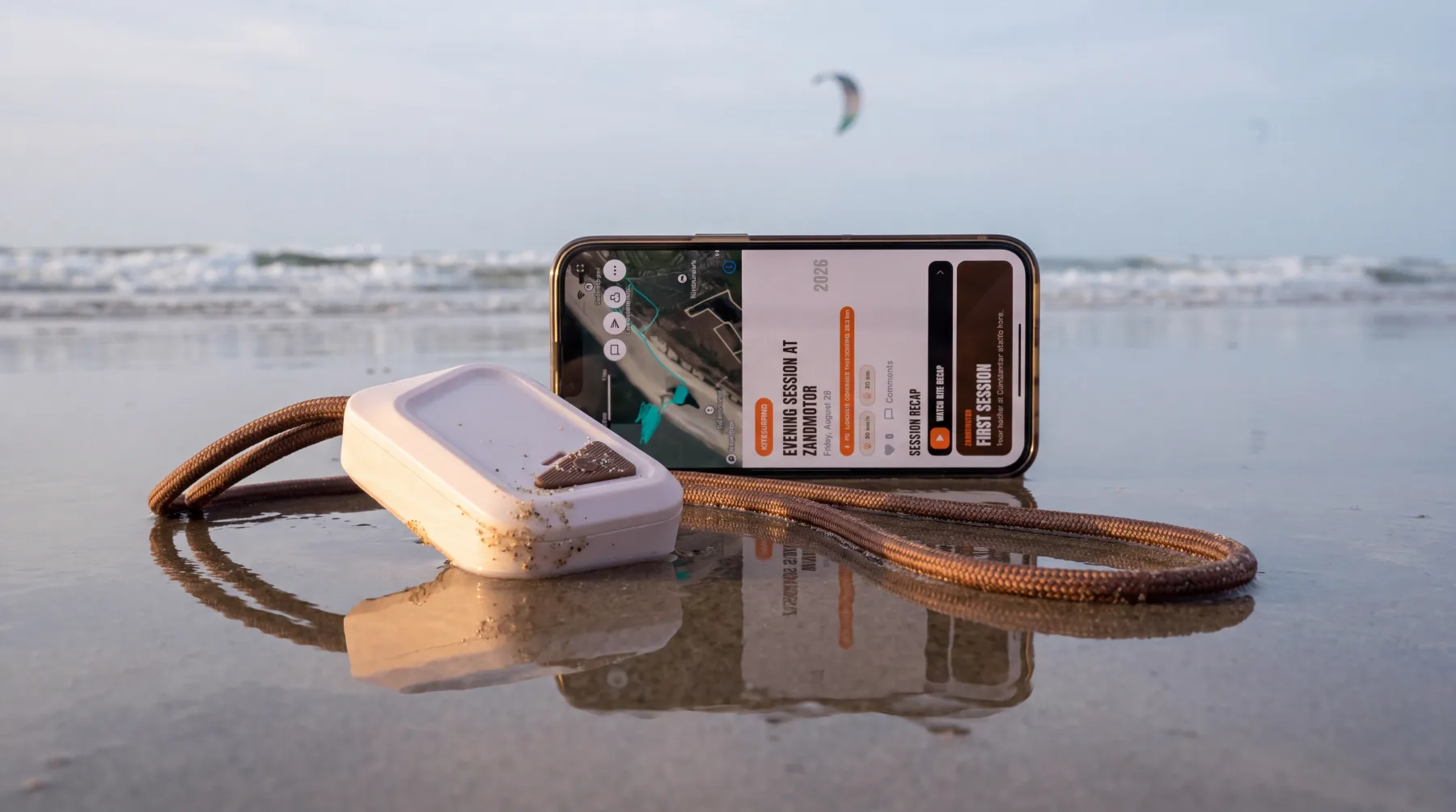 SANDIT Sensor and the app on the beach, a kitesurfer on the water behind